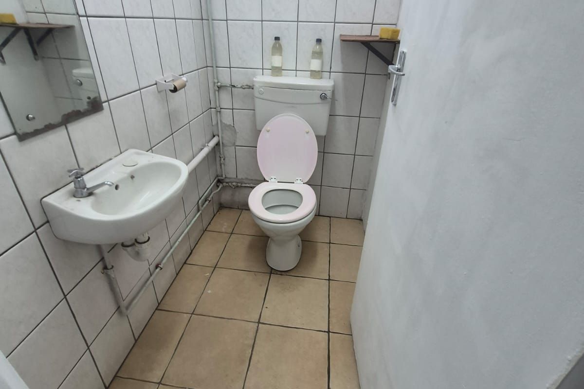A compact bathroom featuring a wall-mounted basin and ceramic toilet with tiled walls and flooring, requiring cosmetic updates to improve the overall finish.