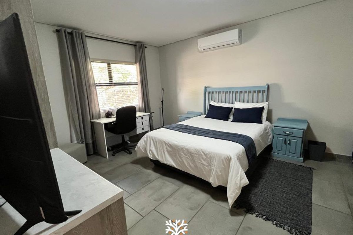 A well-maintained bedroom featuring tiled flooring, a wall-mounted air conditioning unit, and large windows providing natural light.