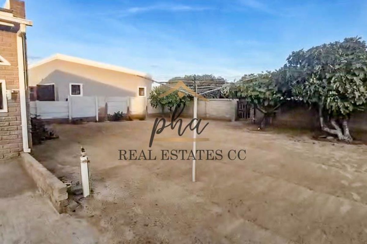 A spacious rear yard area featuring perimeter boundary walls and established trees, offering potential for landscaping or outdoor development.