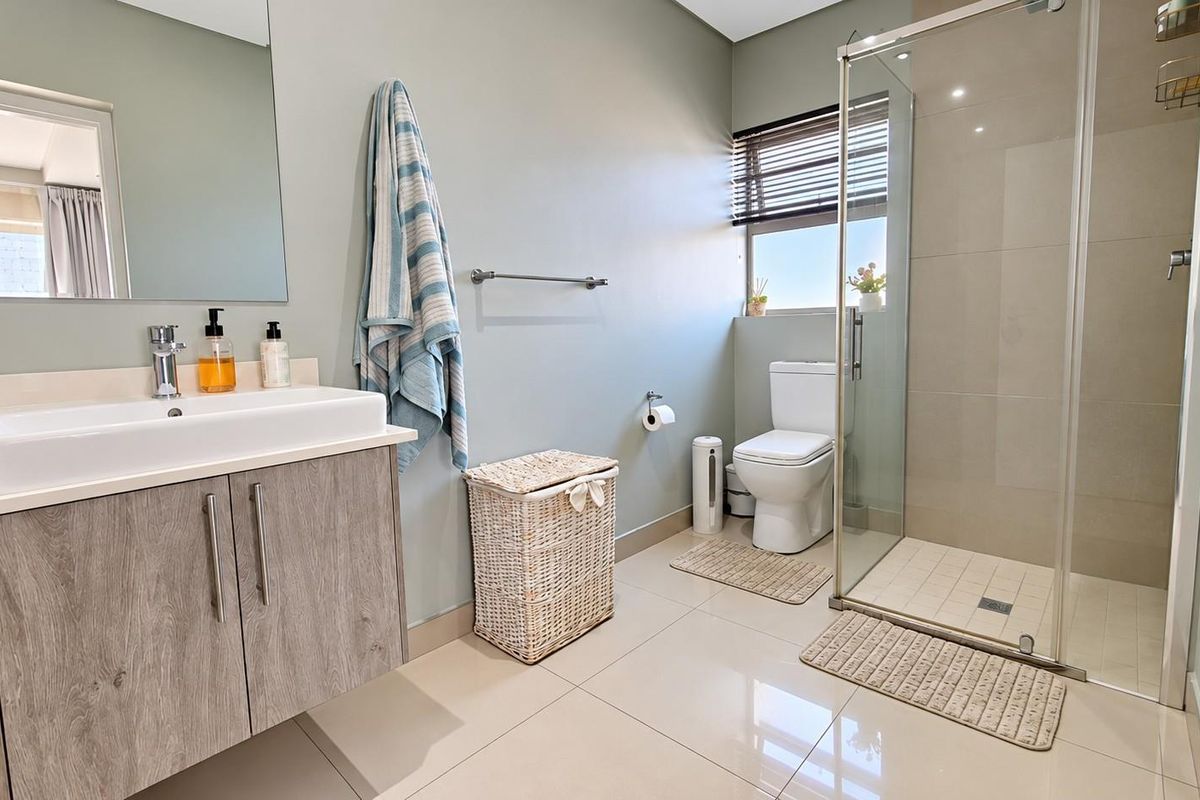 Modern bathroom featuring a vanity cabinet with basin, glass-enclosed shower, and neutral tiled finishes, offering a clean and functional space.