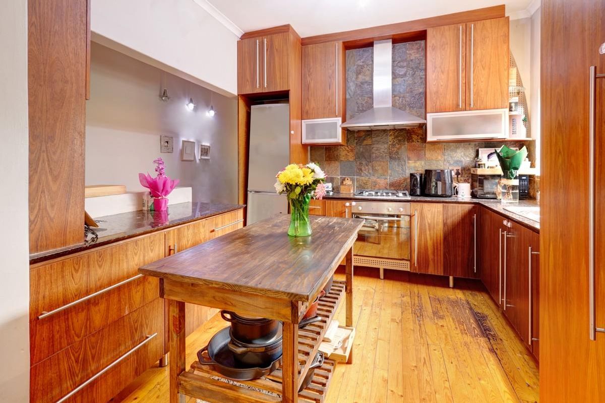 A well-appointed kitchen featuring warm wood cabinetry, granite countertops, a stone tile backsplash, and high-quality stainless steel appliances, complemented by rich hardwood flooring.