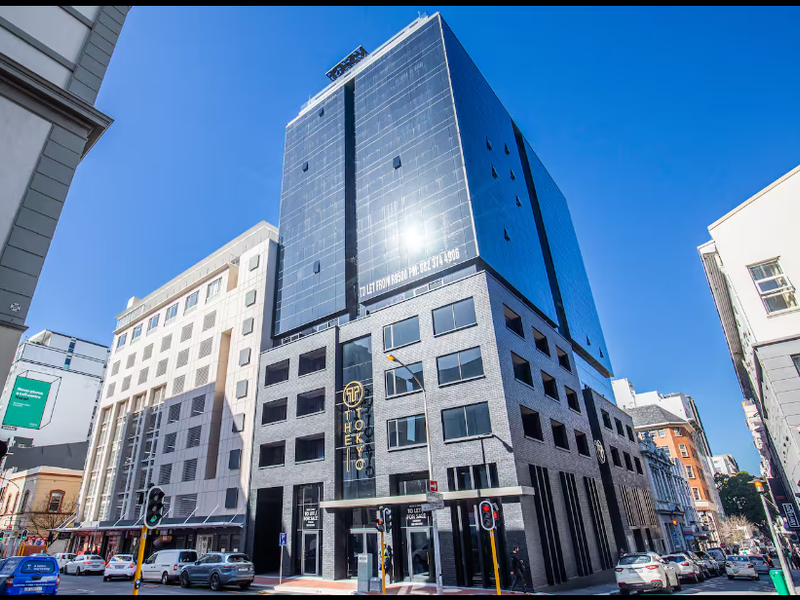 Modern high-rise apartment building featuring a glass facade and brick exterior, located in a busy urban street setting.