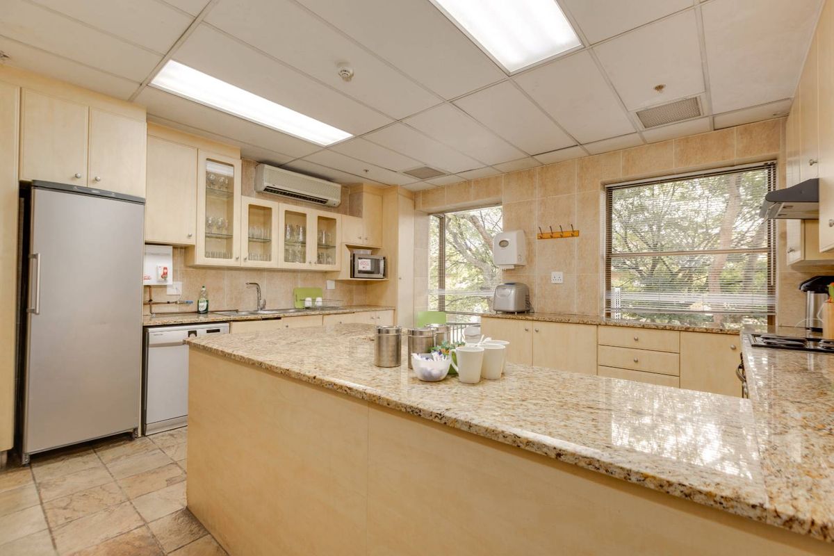 A functional office kitchen featuring granite countertops, ample built-in cabinetry, tiled finishes, and integrated lighting, providing a practical space for staff amenities.