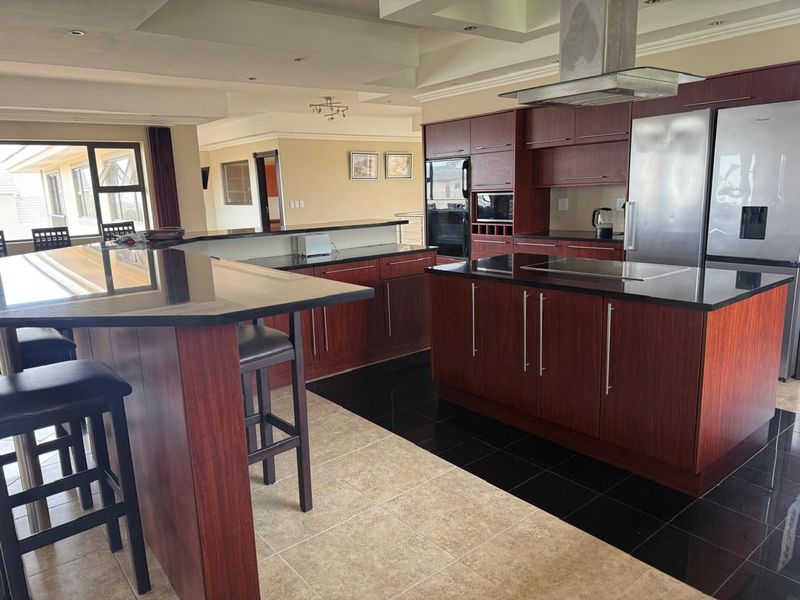 Spacious kitchen featuring dark wood cabinetry, granite countertops, a central island, and modern built-in appliances with a coffered ceiling design.