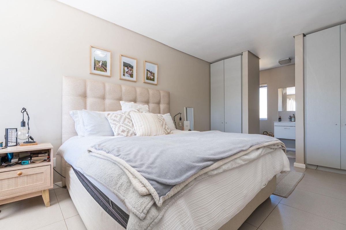 A well-maintained bedroom featuring neutral tones, built-in cupboards, and direct access to an en-suite bathroom with tiled flooring throughout.