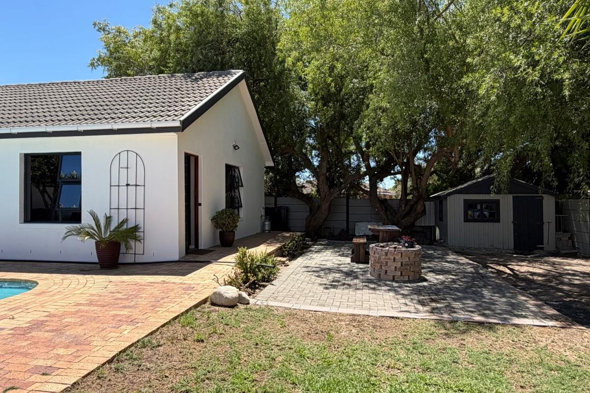 A rear garden area featuring a paved patio, a brick fire pit, a swimming pool, and a detached storage shed.