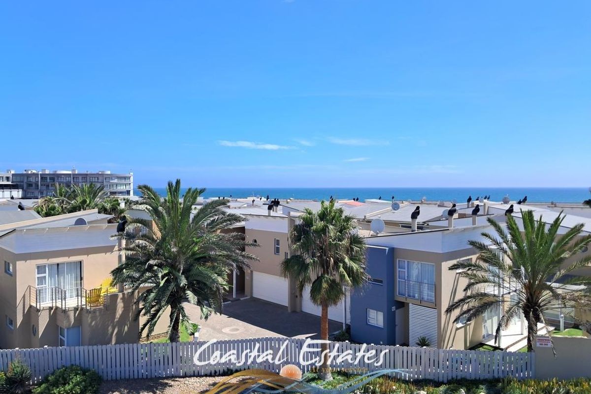 Elevated aerial view of a coastal residential complex featuring modern townhouses, paved driveways, and landscaped palm trees under a clear blue sky.