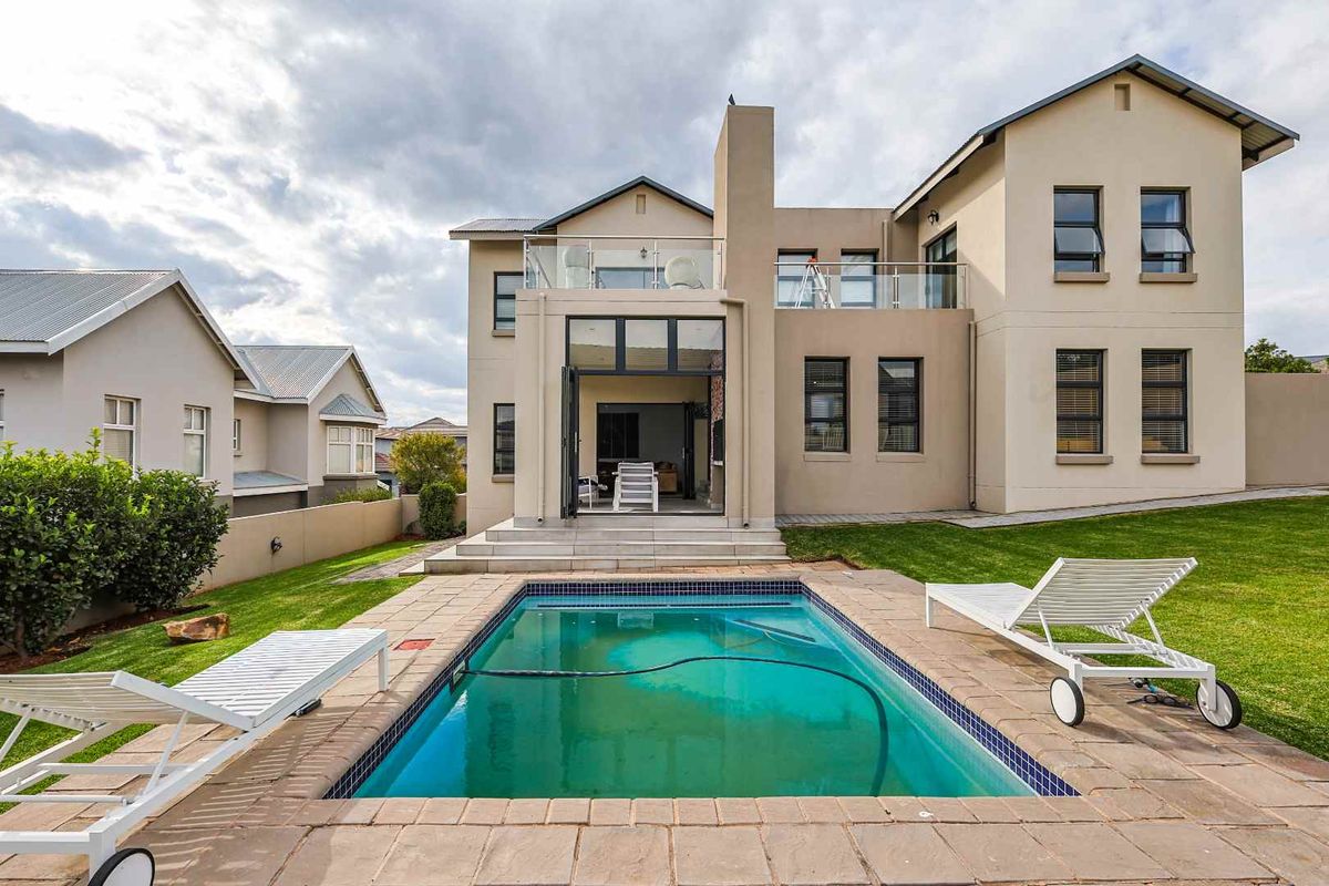Rear view of a two-story house featuring a swimming pool, paved patio area, and a balcony accessible from the upper level.