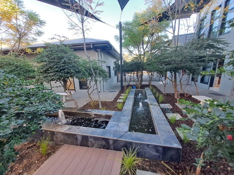 A well-maintained office courtyard featuring a modern tiled water feature, paved walkways, and established landscaping between office buildings.