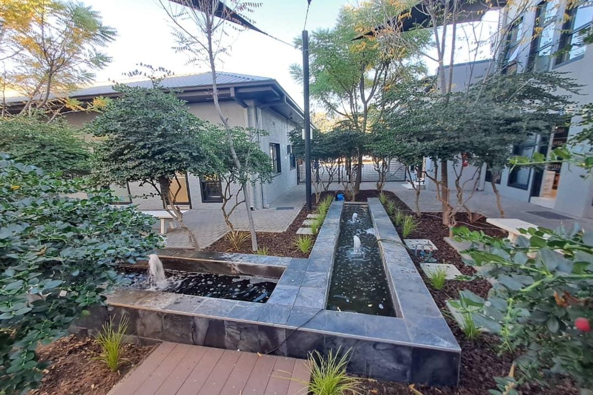 A well-maintained office courtyard featuring a modern tiled water feature, paved walkways, and established landscaping between office buildings.