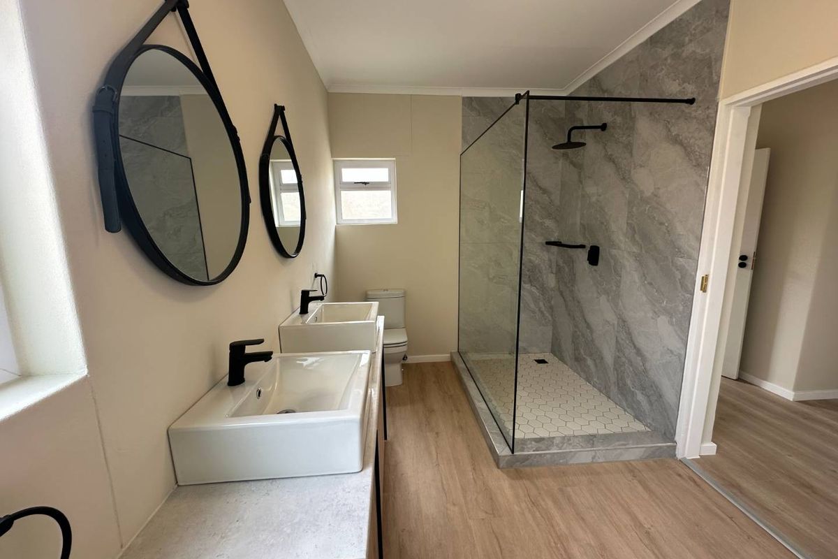 Modern bathroom featuring a double vanity with black tapware, a spacious walk-in shower with grey marble-look tiling, and light wood-look flooring.