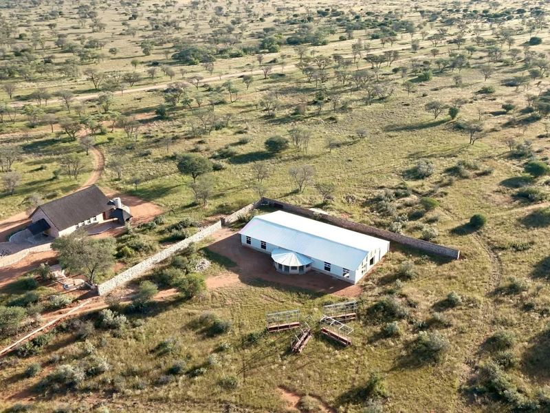 Aerial view of a rural property featuring two main structures, stone boundary walls, and expansive natural landscape.