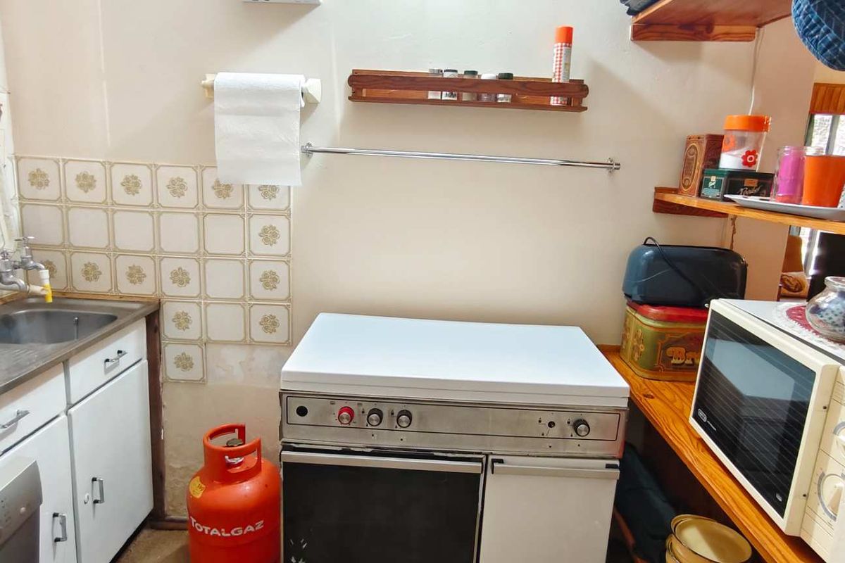A compact, functional kitchen area featuring a stainless steel sink, gas stove, and open timber shelving for storage.