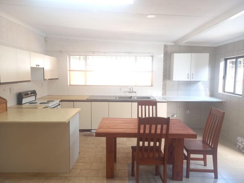 A functional kitchen featuring built-in cabinetry, laminate countertops, a double sink, and an electric stove, with tiled flooring and splashbacks throughout.