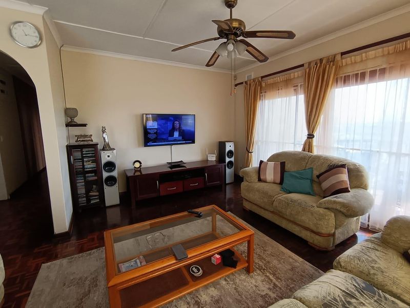 A comfortable living room featuring classic parquet flooring, a ceiling fan, and large sliding glass doors that provide natural light.