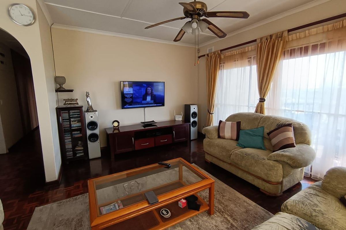 A comfortable living room featuring classic parquet flooring, a ceiling fan, and large sliding glass doors that provide natural light.