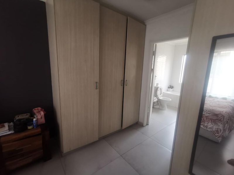 A bedroom featuring light wood-finish built-in cupboards, tiled flooring, and direct access to an en-suite bathroom.