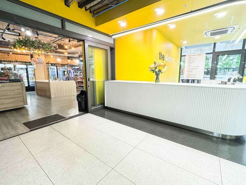 Modern commercial reception area featuring a sleek white counter, vibrant yellow accent wall, and polished tiled flooring with integrated lighting.