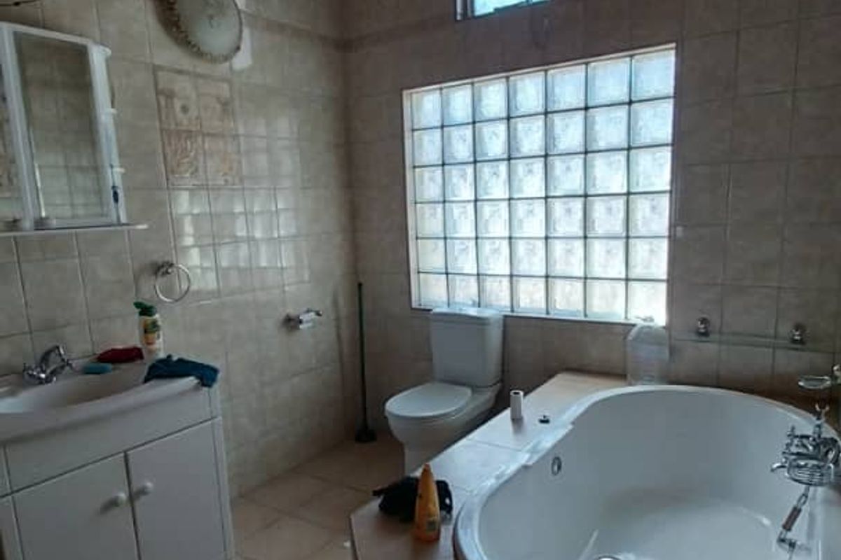 A bathroom featuring a built-in corner bathtub, vanity cabinet with sink, toilet, and glass block window, finished with tiled walls and a timber ceiling.