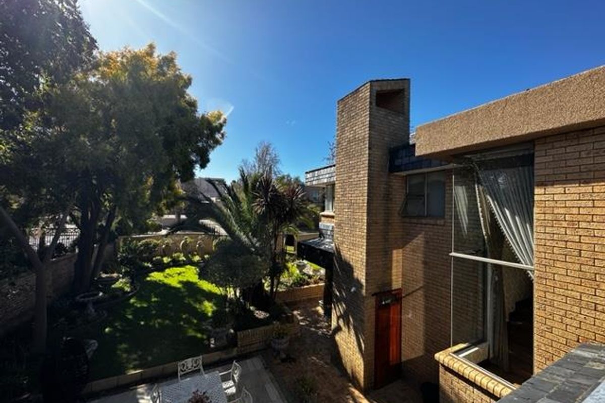 A view of the rear garden and patio area, featuring established landscaping, brick facade, and a prominent chimney structure.