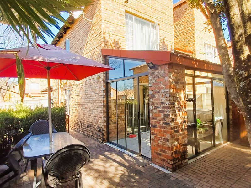 Rear view of a townhouse featuring an exposed brick facade, a paved patio area, and modern sliding glass doors leading into the home.