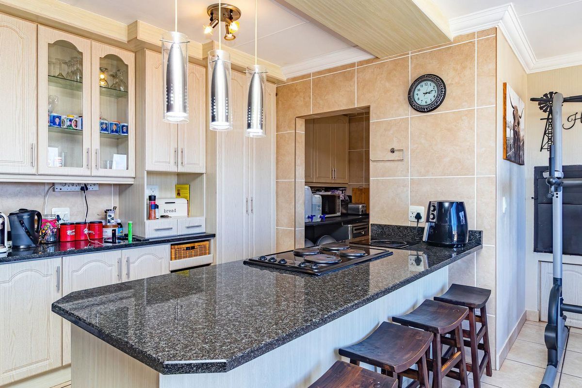 A functional kitchen featuring granite countertops, a built-in hob, ample cabinetry, and a breakfast bar, with an adjacent scullery area.