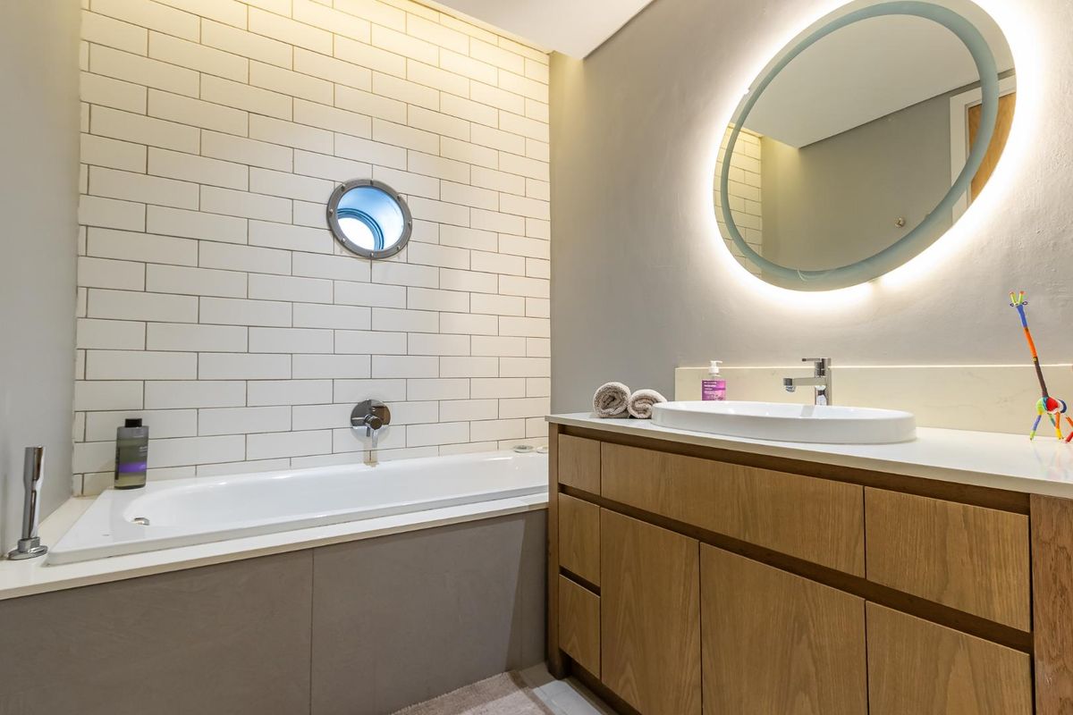 Modern bathroom featuring a built-in bathtub, subway tile wall cladding, a circular porthole window, and a contemporary wooden vanity with an integrated basin.