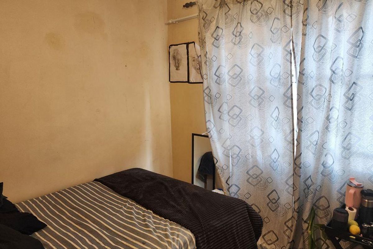 A bedroom featuring a window with patterned curtains and visible wall staining, requiring cosmetic attention.