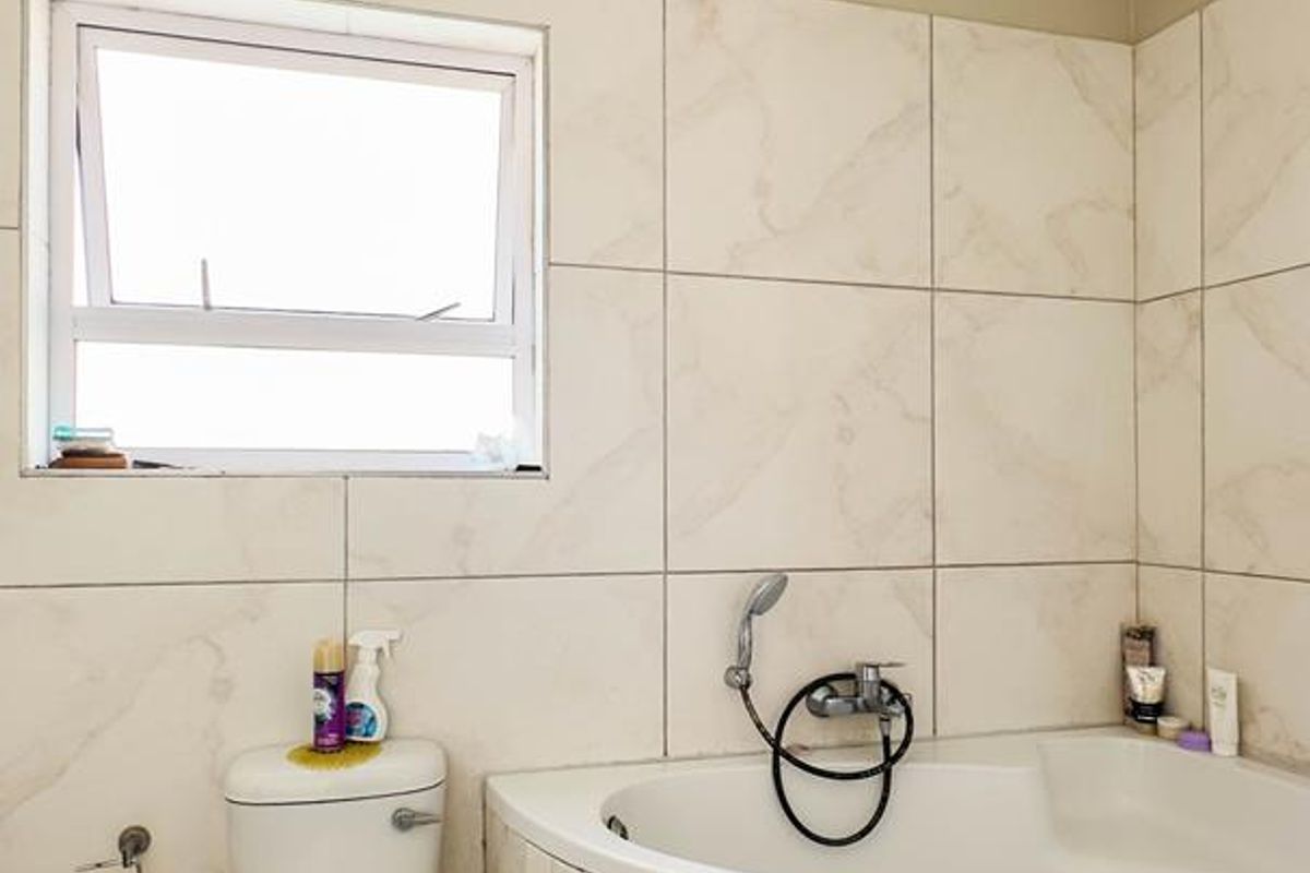A functional bathroom featuring a corner bathtub with a handheld shower attachment and a standard toilet, finished with neutral wall and floor tiling.