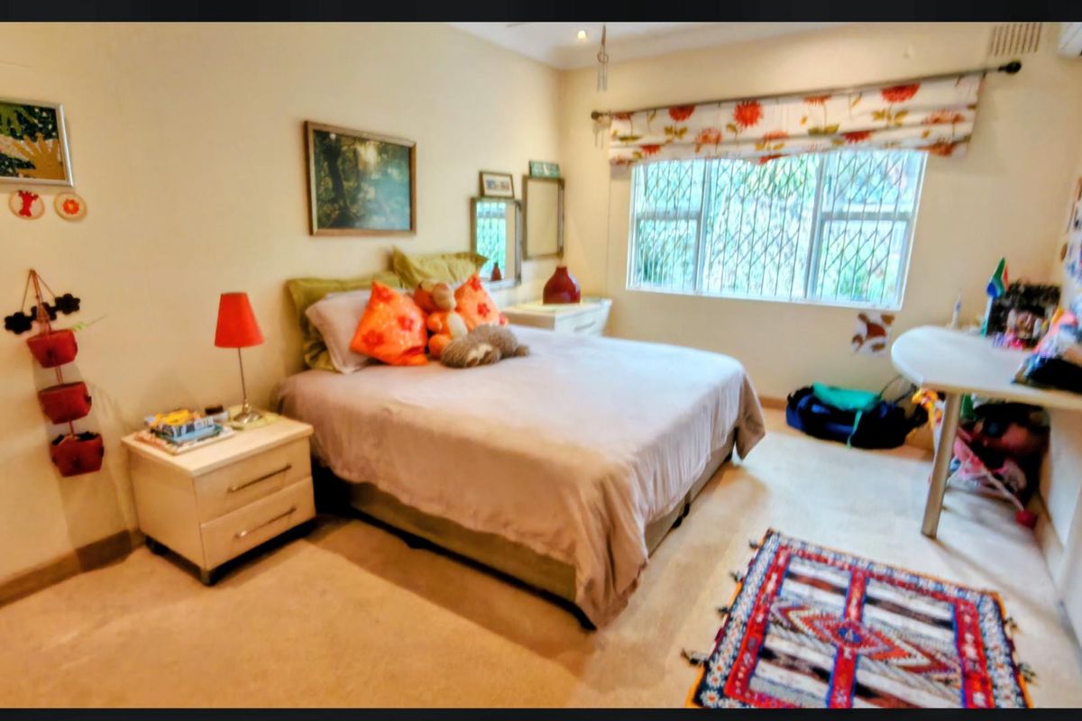 A carpeted bedroom featuring security bars on the window and a built-in air conditioning unit.