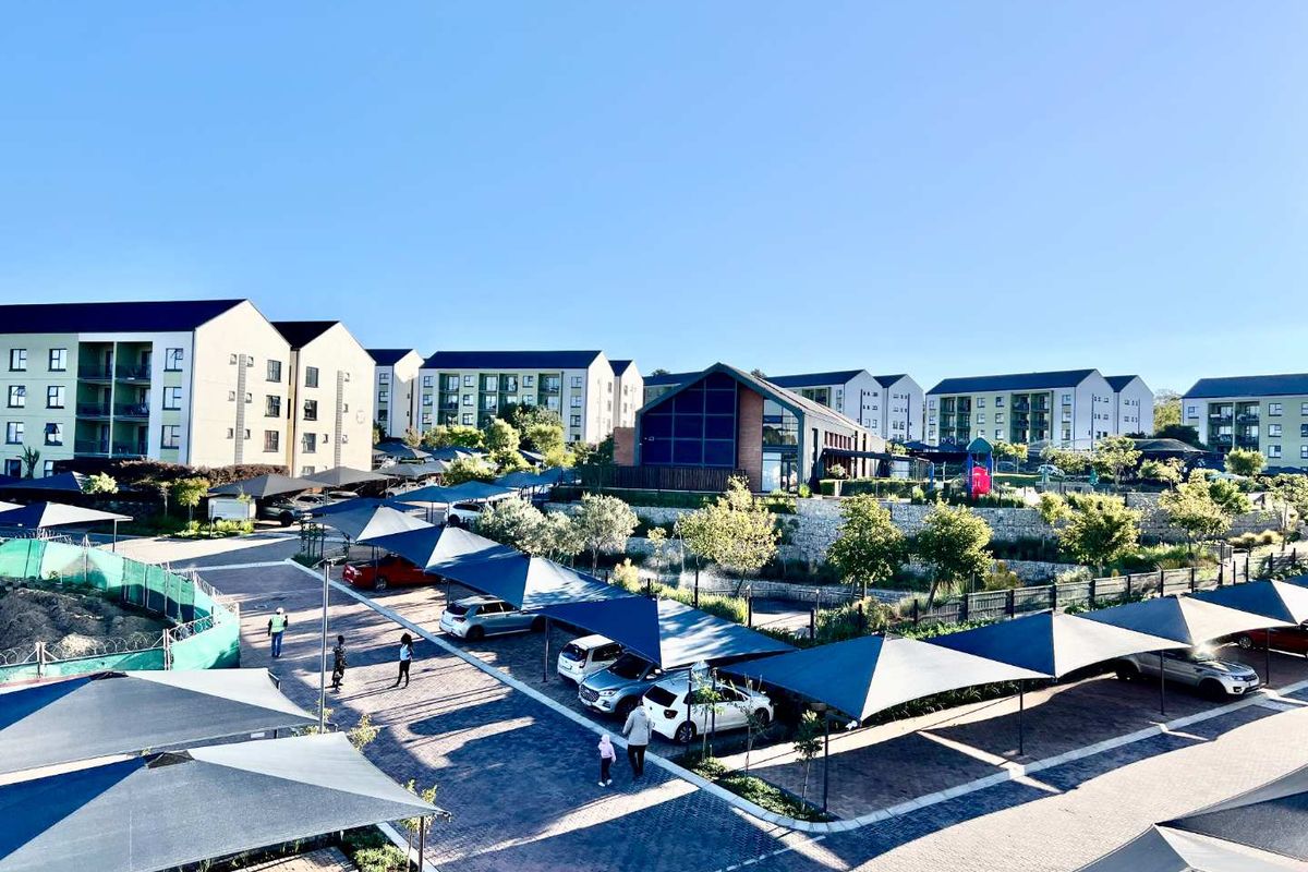 An elevated view of a modern apartment complex featuring paved parking areas with shade sail structures and landscaped grounds.
