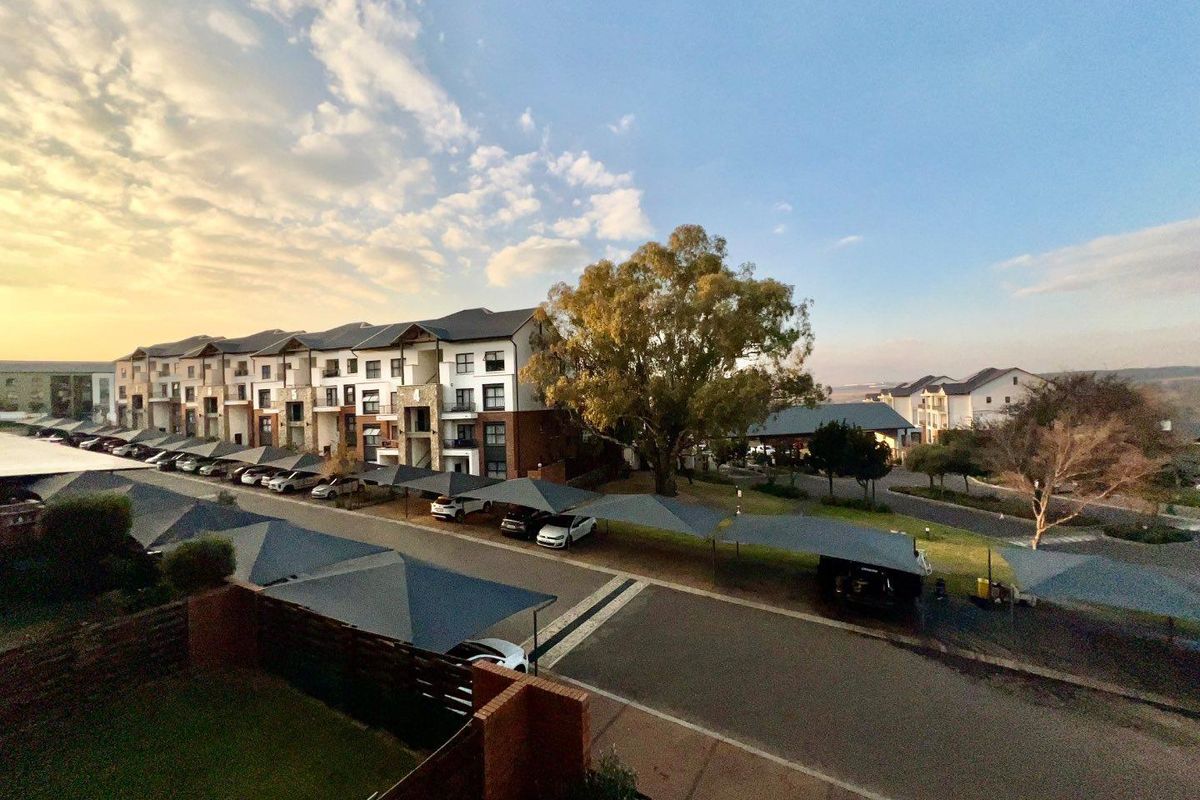 An elevated aerial view of the apartment complex grounds, featuring paved driveways, structured shade cloth carports, and well-maintained landscaped areas.