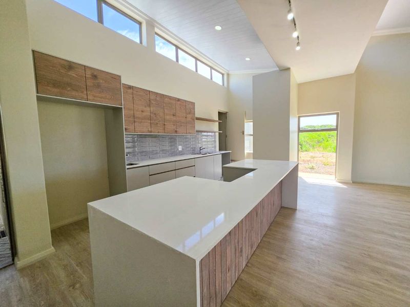 Modern open-plan kitchen featuring a large island with quartz countertops, wood-finish cabinetry, and high clerestory windows providing ample natural light.