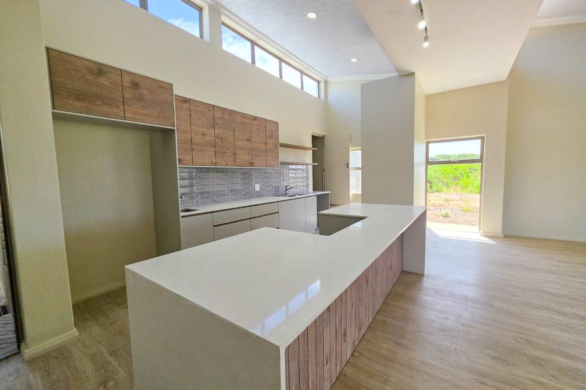 Modern open-plan kitchen featuring a large island with quartz countertops, wood-finish cabinetry, and high clerestory windows providing ample natural light.
