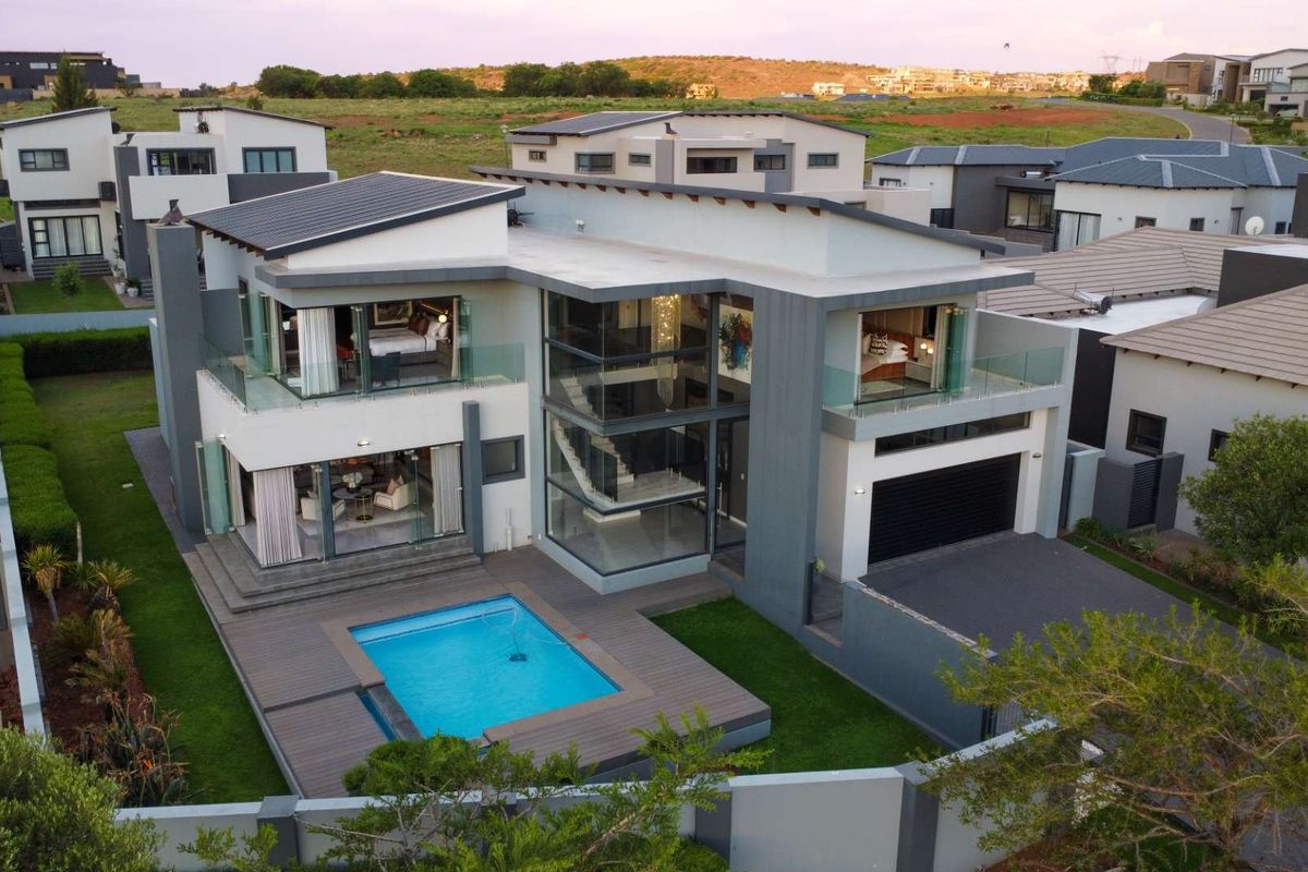 Aerial view of a modern two-story residence featuring a swimming pool, expansive glass facade, balcony areas, and a double garage.