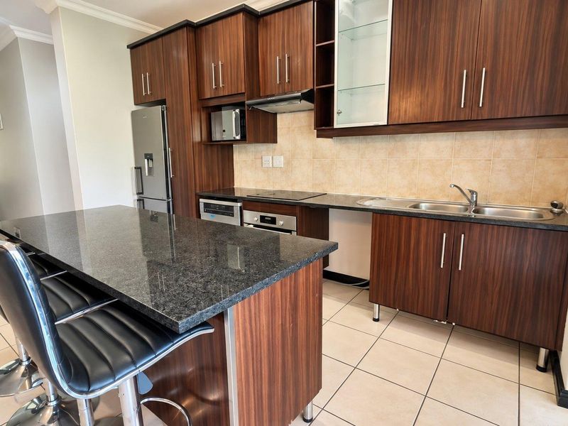 Modern kitchen featuring dark wood cabinetry, granite countertops, a central island, and integrated appliances, offering a functional and stylish cooking space.