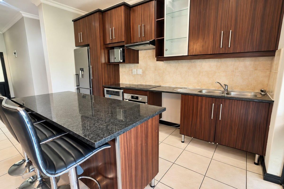 Modern kitchen featuring dark wood cabinetry, granite countertops, a central island, and integrated appliances, offering a functional and stylish cooking space.