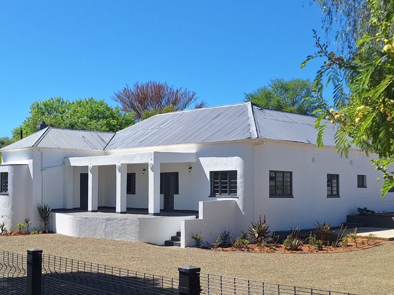 A well-maintained single-story guest house featuring a white rendered facade, corrugated metal roof, and a covered front porch with concrete pillars.