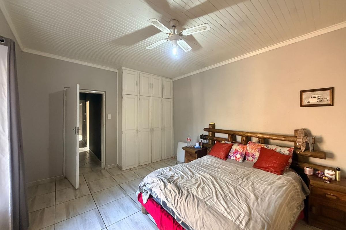 A bedroom featuring tiled flooring, a timber-look ceiling with a central fan, and built-in storage cupboards.