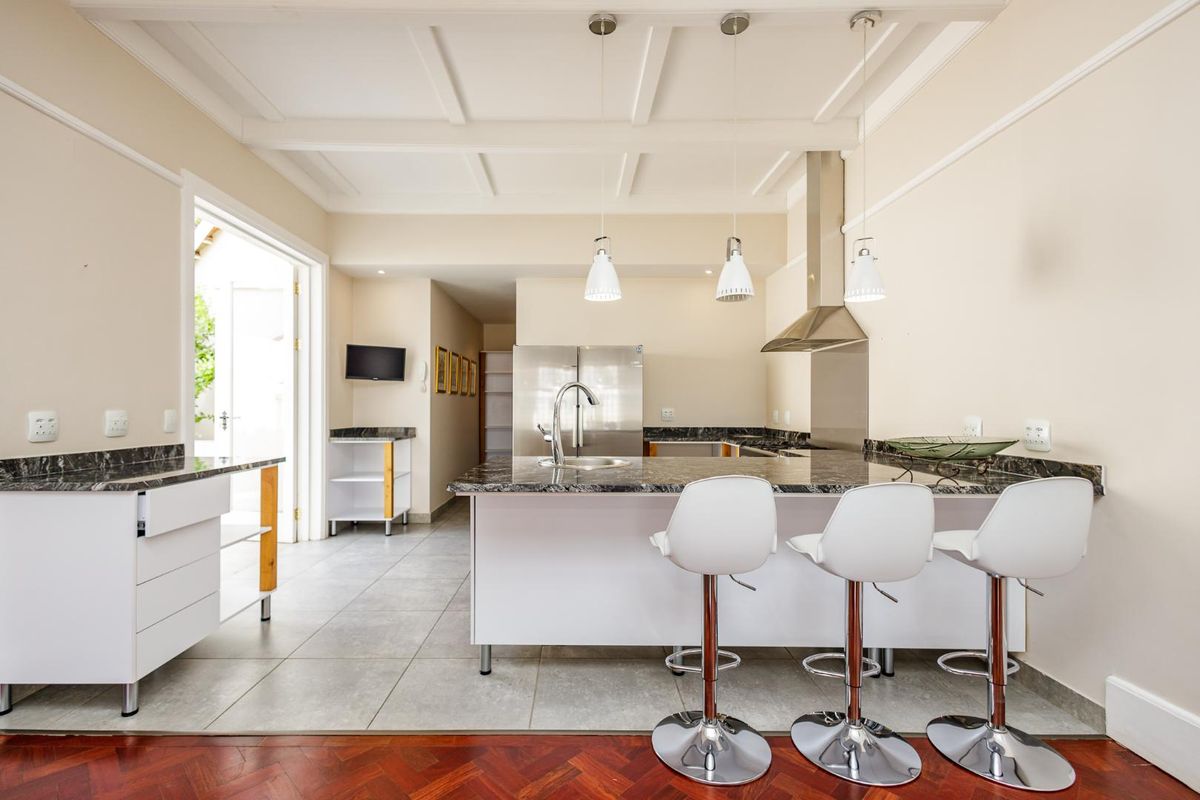 Modern kitchen featuring a central island with granite countertops, stainless steel extractor fan, and elegant coffered ceilings, opening onto an outdoor area.