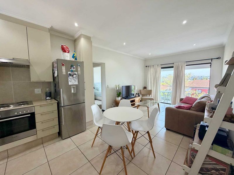 Open-plan living area featuring a modern kitchen with built-in appliances, tiled flooring, and direct access to a balcony with scenic views.