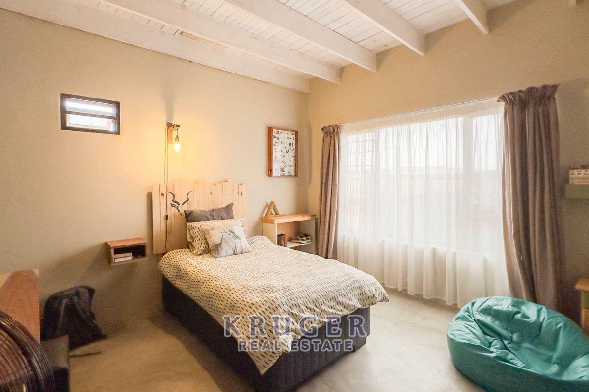 A bedroom featuring exposed white-painted timber ceiling beams, neutral wall finishes, and a large window allowing for natural light.