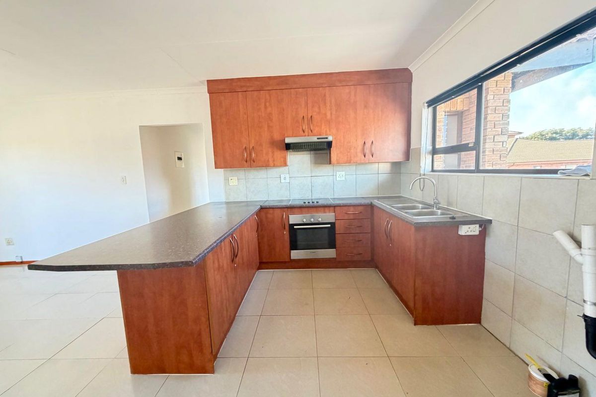 A functional kitchen featuring wood-look cabinetry, laminate countertops, built-in oven, hob, extractor fan, and a double bowl sink with tiled splashbacks.