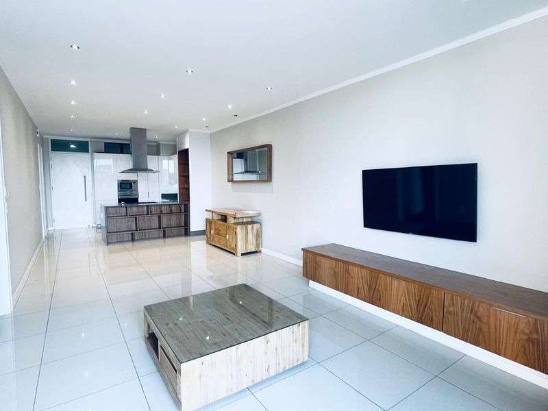 Modern open-plan living area featuring high-gloss floor tiles, recessed lighting, and a sleek kitchen with integrated appliances and contemporary cabinetry.