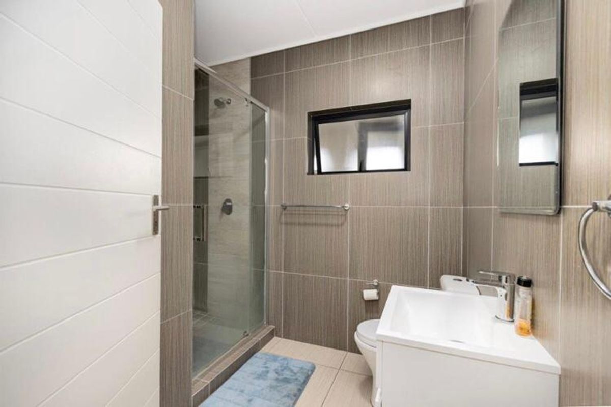 Modern bathroom featuring a glass-enclosed shower, wall-mounted vanity with mixer tap, and neutral floor-to-ceiling wall tiling.