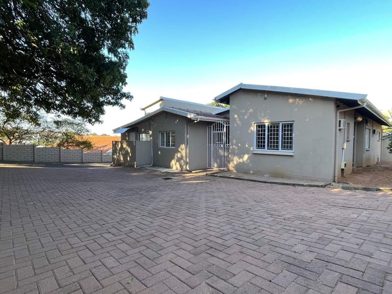 Front exterior view of the house featuring a large paved driveway, security gates, and perimeter walling.