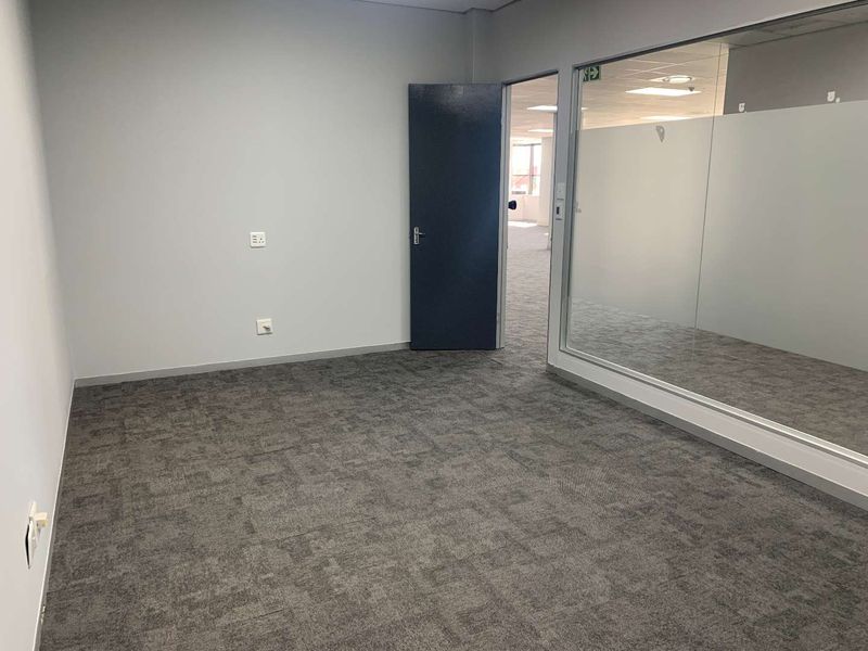 A clean, empty office space featuring grey carpet tiles, a glass partition wall, and neutral wall finishes, ready for professional fit-out.