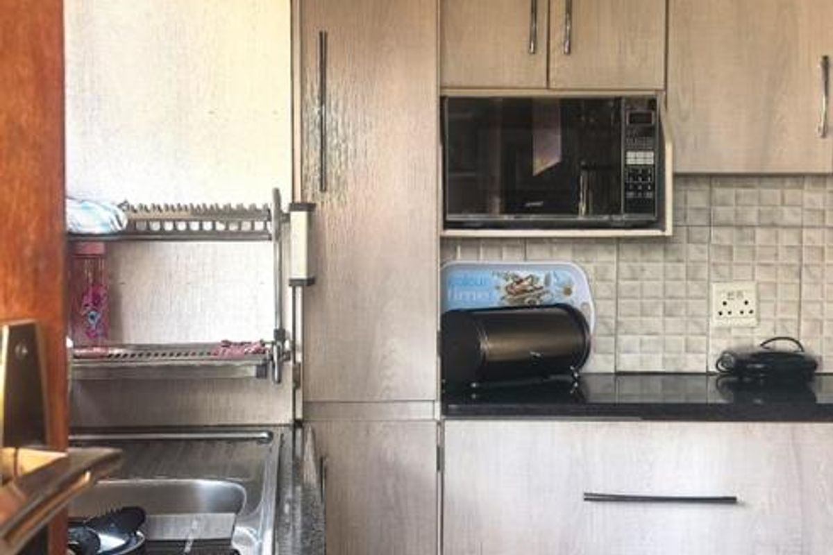 A compact kitchen featuring light wood-grain cabinetry, dark granite countertops, a built-in microwave, and tiled flooring.