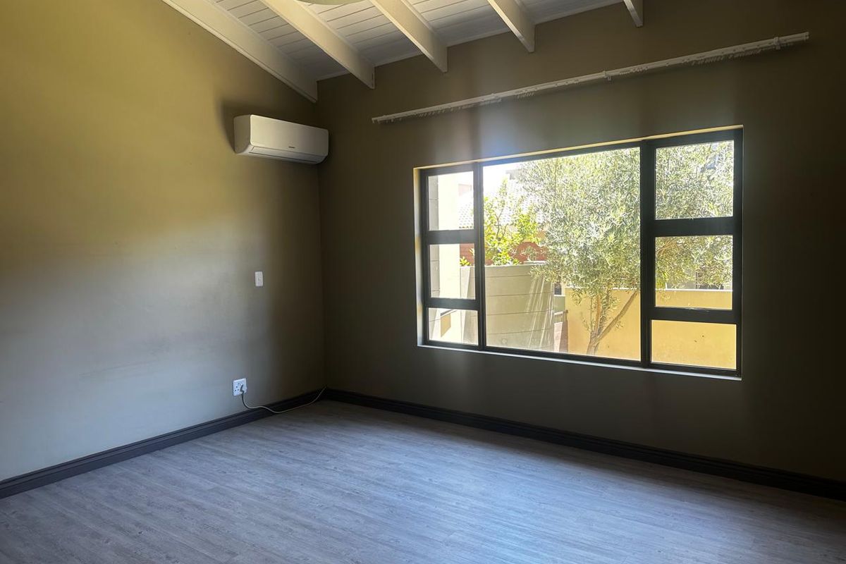 A bright, empty bedroom featuring vaulted ceilings with exposed beams, wood-look laminate flooring, and a wall-mounted air conditioning unit.