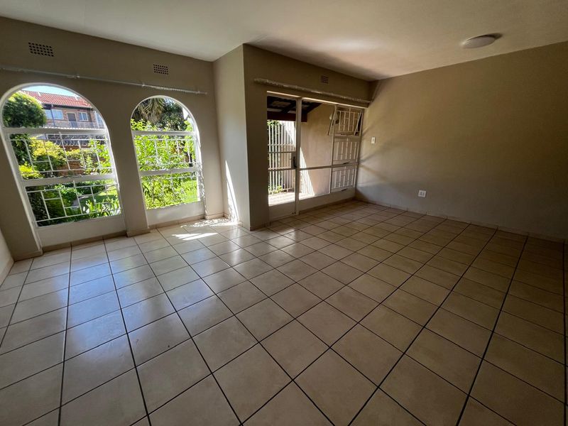 Spacious, empty living area featuring neutral tiled flooring, distinctive arched windows, and direct access to an outdoor patio through a sliding glass door.